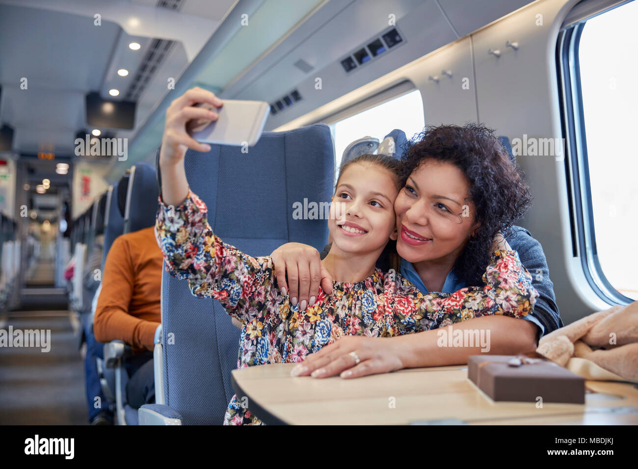 Affectionate mother and daughter taking selfie with camera phone on passenger train Stock Photo