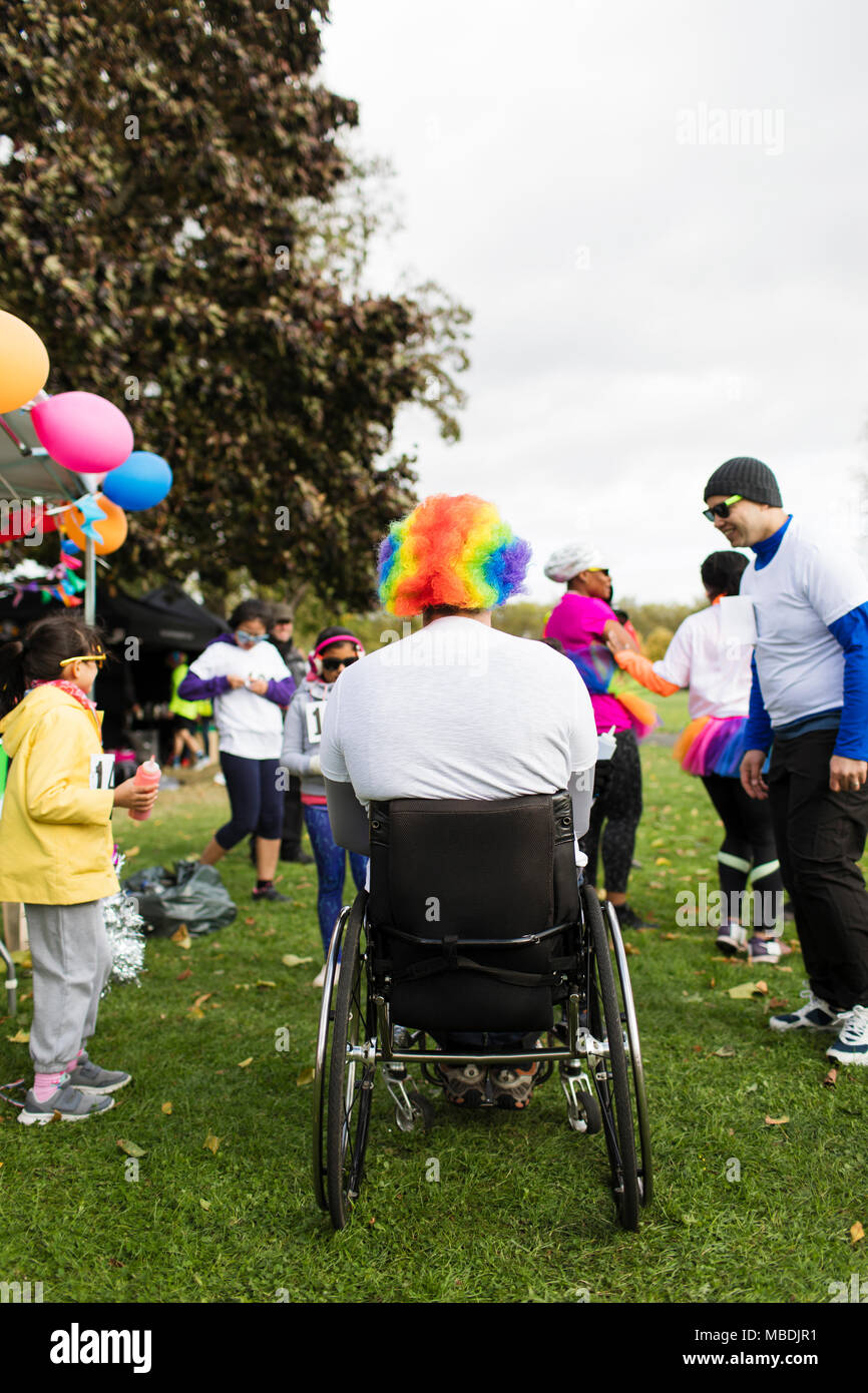 Man in wheelchair wearing clown wig at charity race in park Stock Photo