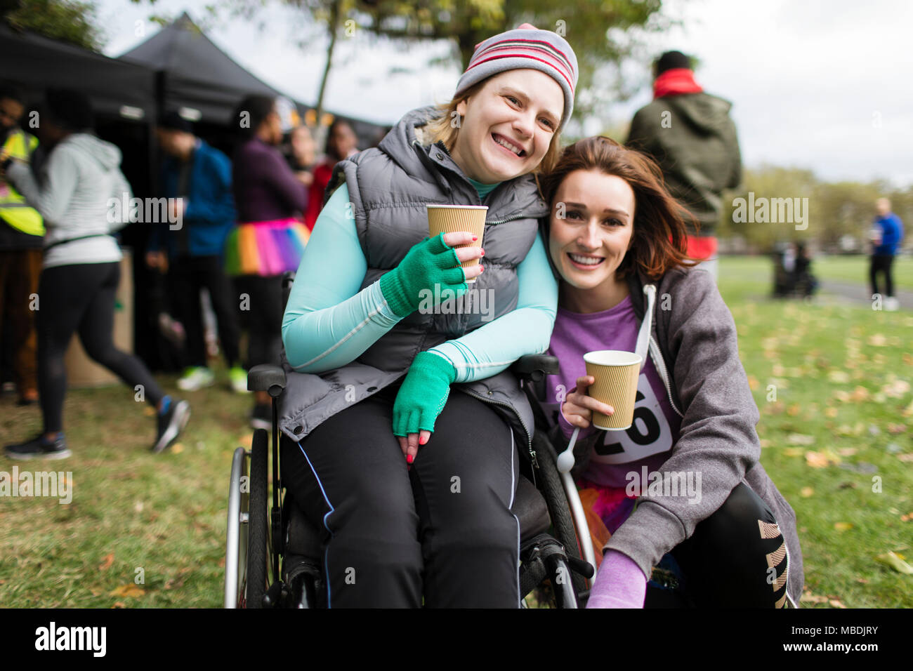 Portrait smiling woman in wheelchair with friend, drinking water at charity race in park Stock Photo