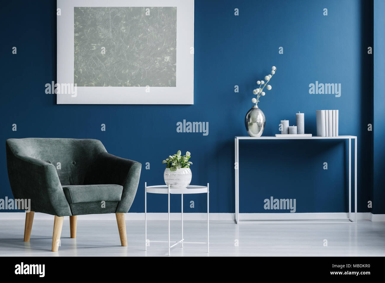 Green armchair against the wall with silver painting in navy blue living room interior with flowers Stock Photo