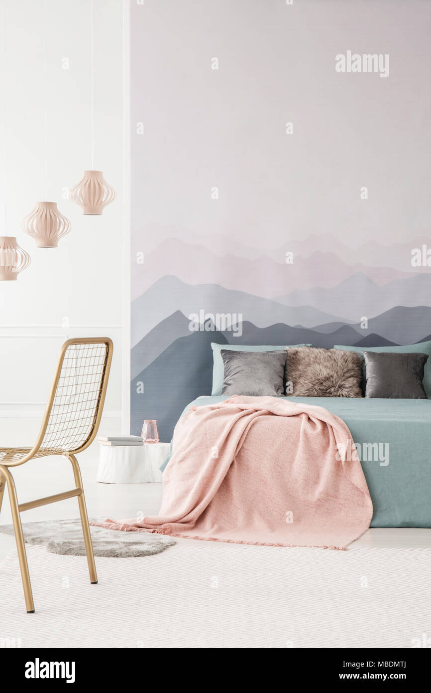 Pink blanket on grey bed in cozy bedroom interior with lamps and gold chair Stock Photo