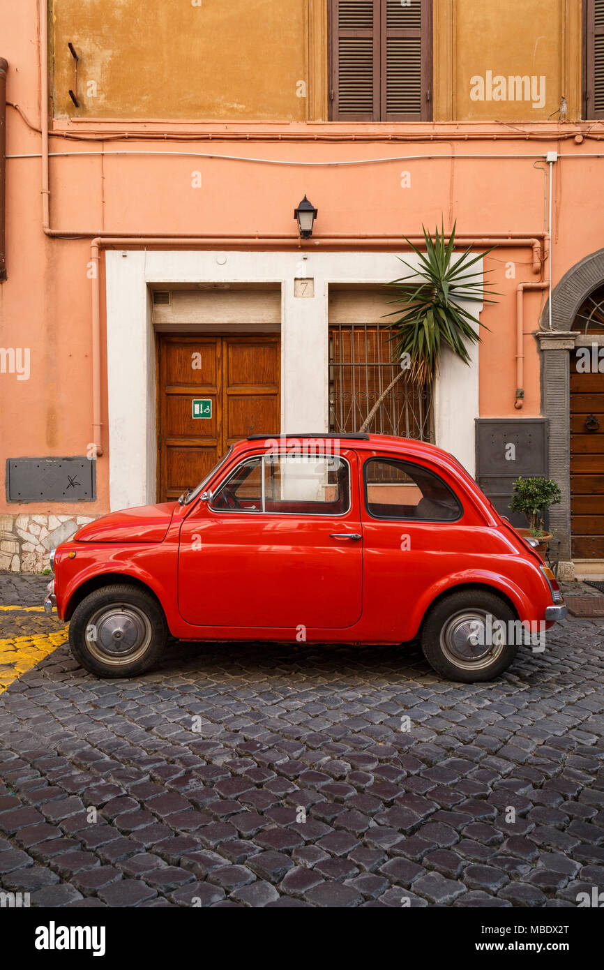 An old red Fiat 500 parked in a cobbled street in Rome, Italy outside a building, the plant is not coming out of the sunroof! Stock Photo