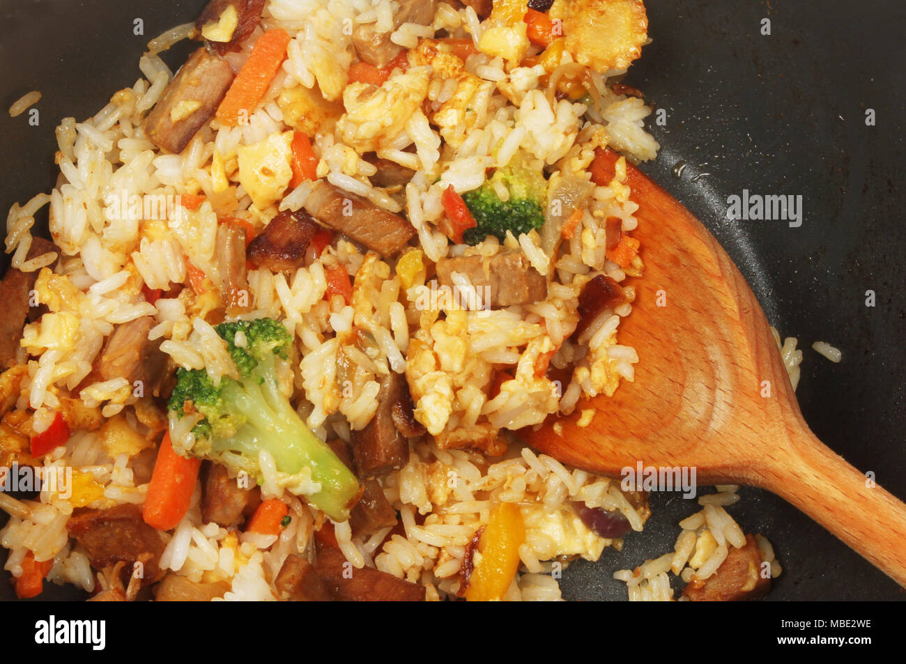 Closeup of fried rice with egg, pork and vegetables in a wok with a wooden spoon Stock Photo