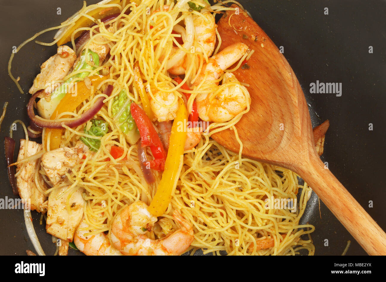 Closeup of a noodle chicken and prawn stir fry with a wooden spoon in a wok Stock Photo