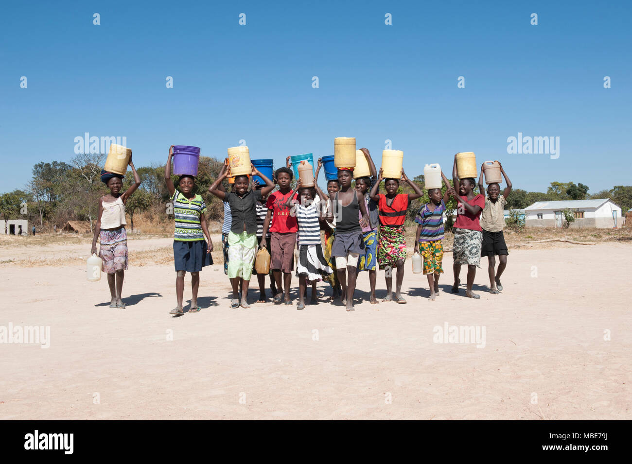 group of Zambian girls carrying water on their heads smiling on sunny day Stock Photo