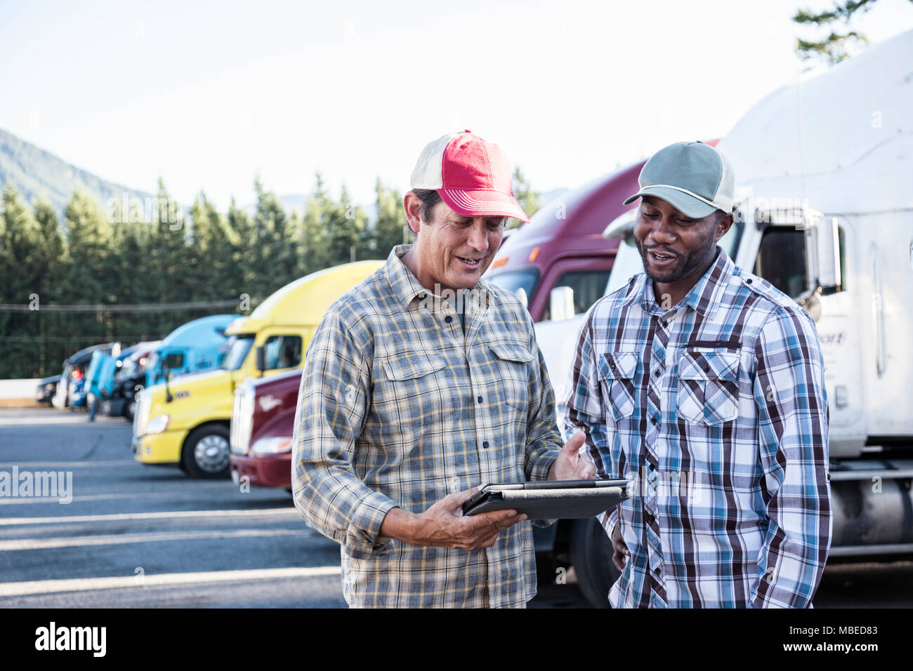A caucasian man and a black man truck driving team together in a truck stop parking lot. Stock Photo