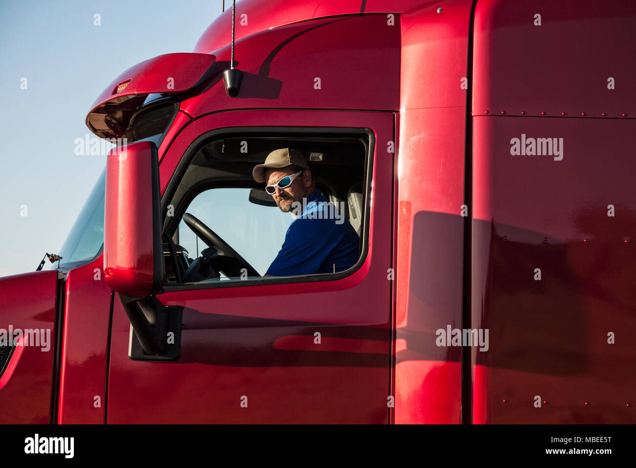 Trucker, truck driver sitting in his cab, at the driving wheel, looking sideways out oif the window. Stock Photo