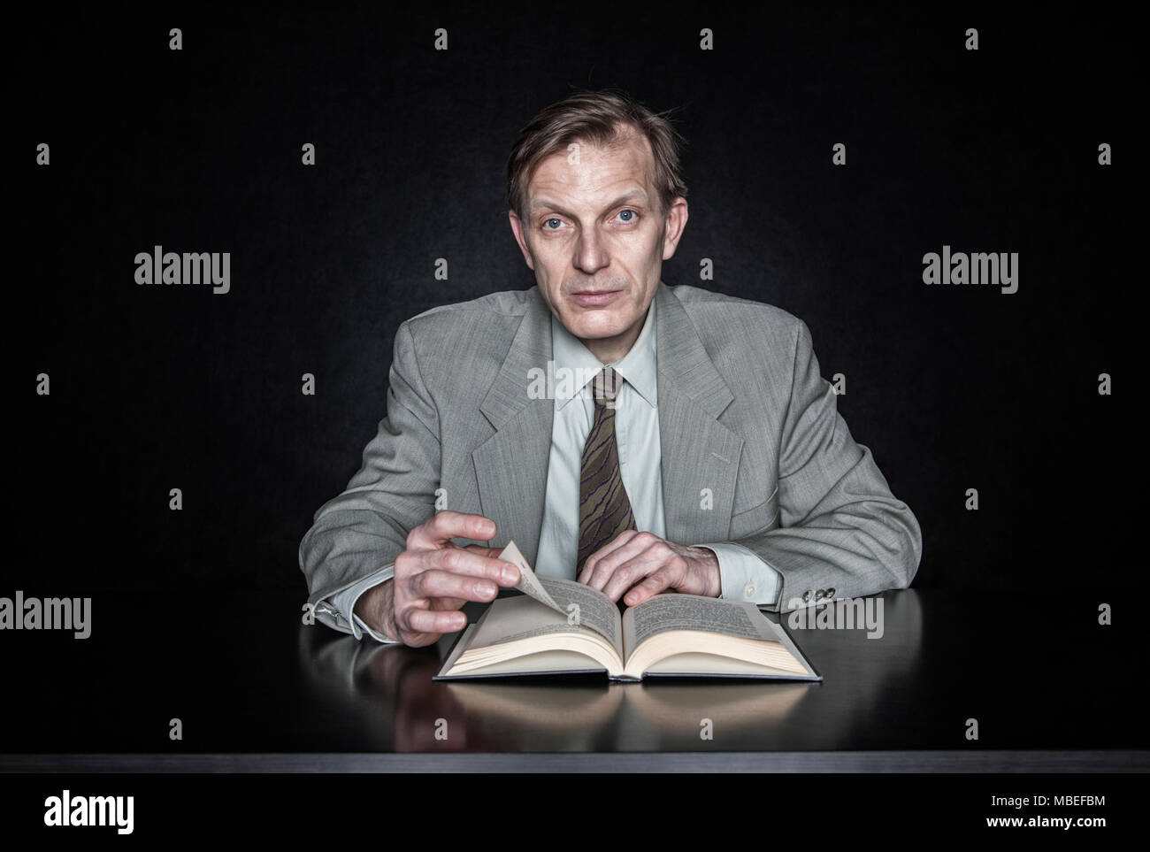 Studio portrait of caucasian man actor seated reading from an open book ...