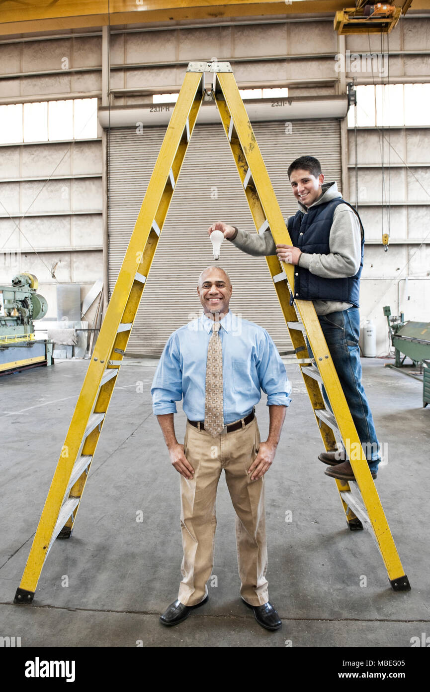 Black man factory owner and young caucasian man factory worker goofing off together on the floor of a sheet metal factory. Stock Photo