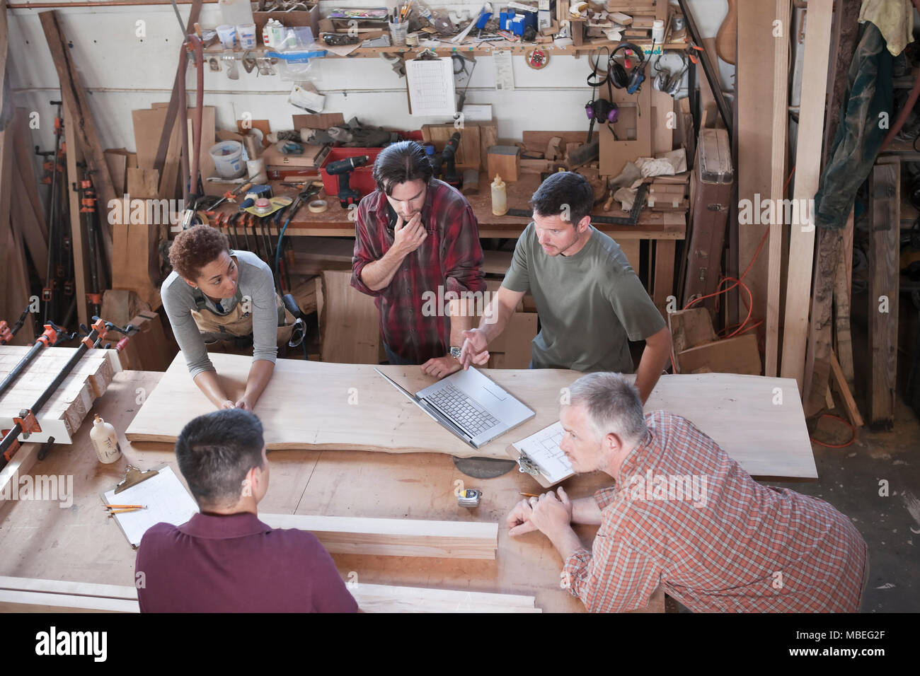 A team of multi-racial factory workers problem solving at a work station in a woodworking factory. Stock Photo