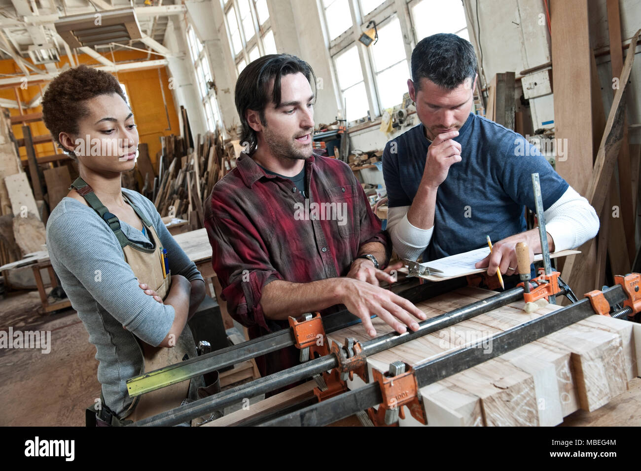 Team of multi-racial workers discussing an issue related to glueing a part together in a woodworking factory. Stock Photo