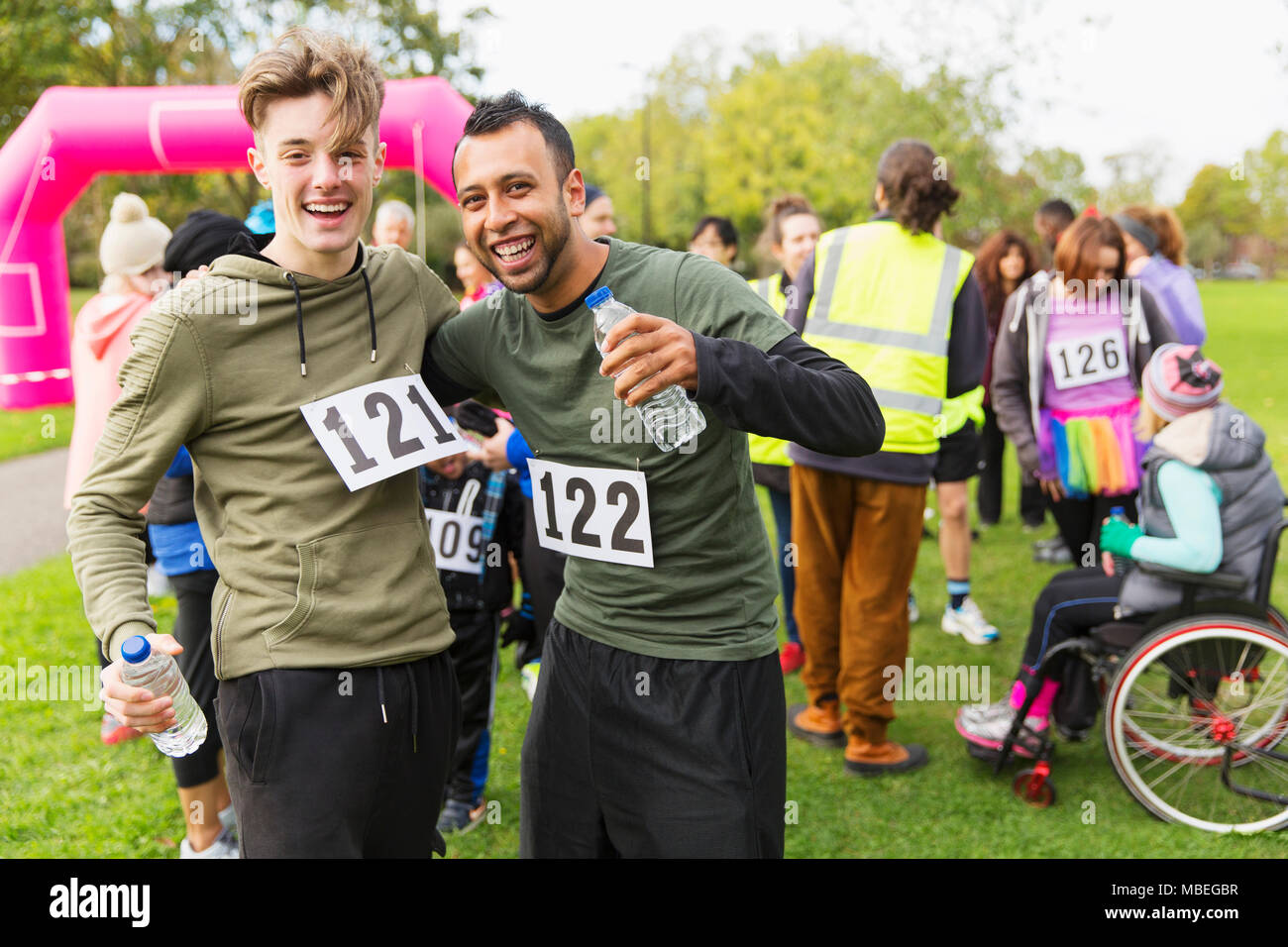 Portrait enthusiastic male runner friends with water hugging at charity run finish line in park Stock Photo