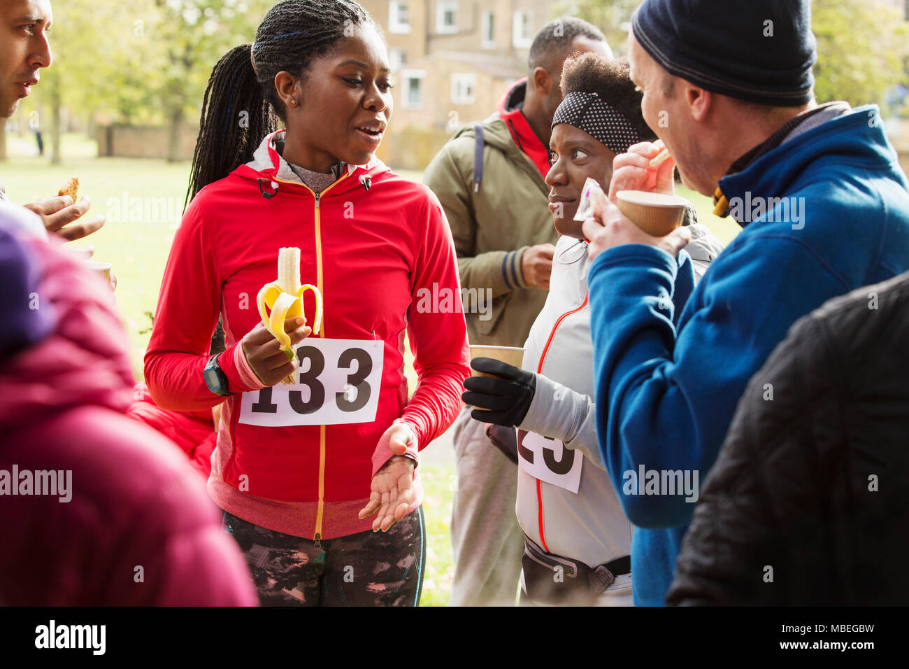 Runners drinking water and eating banana at charity race in park Stock Photo
