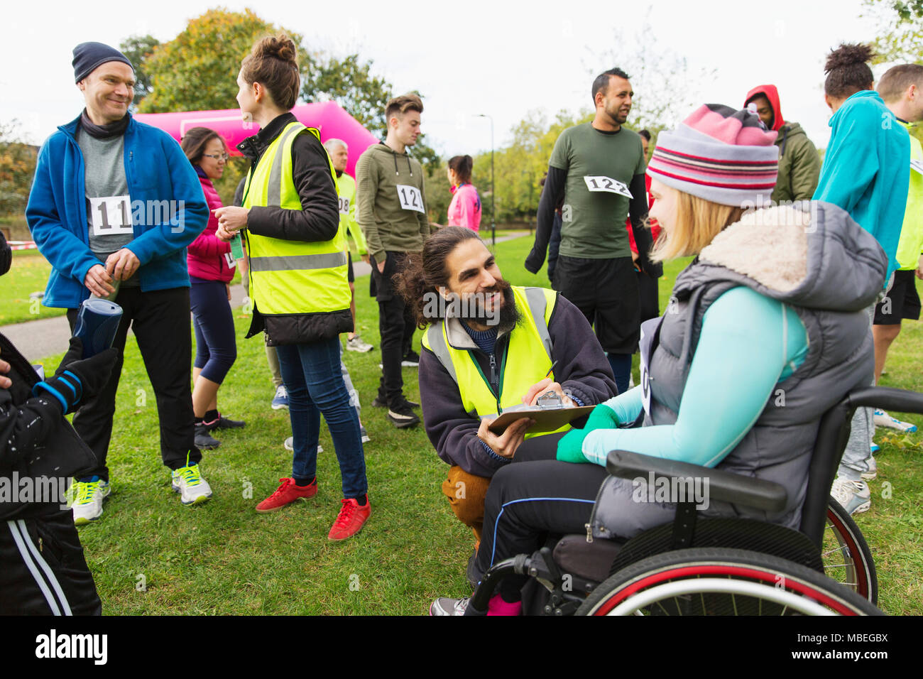 Woman in wheelchair checking in with volunteer at charity race in park Stock Photo
