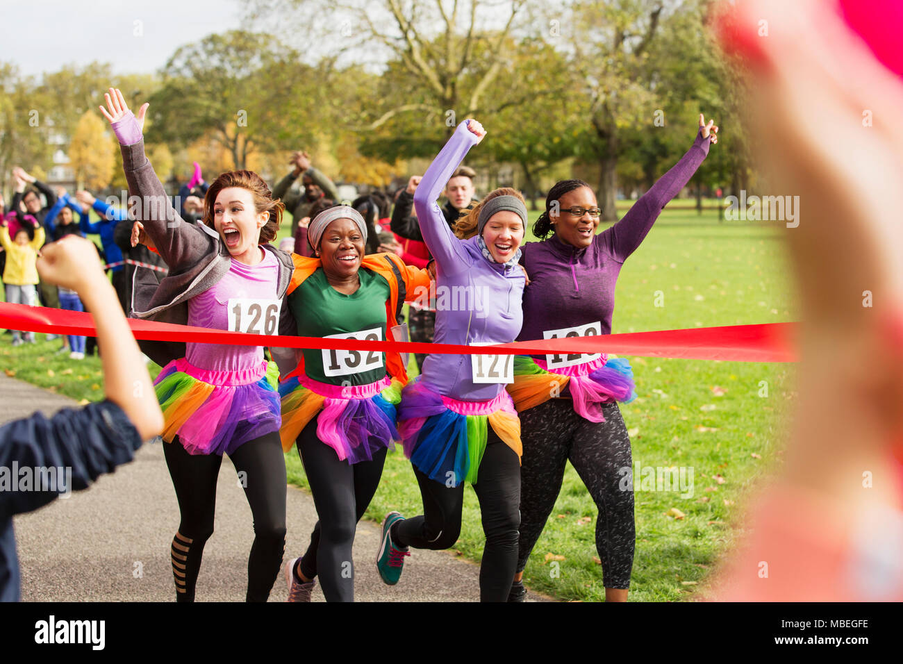 Enthusiastic female runners in tutus crossing charity run finish line in park, celebrating Stock Photo