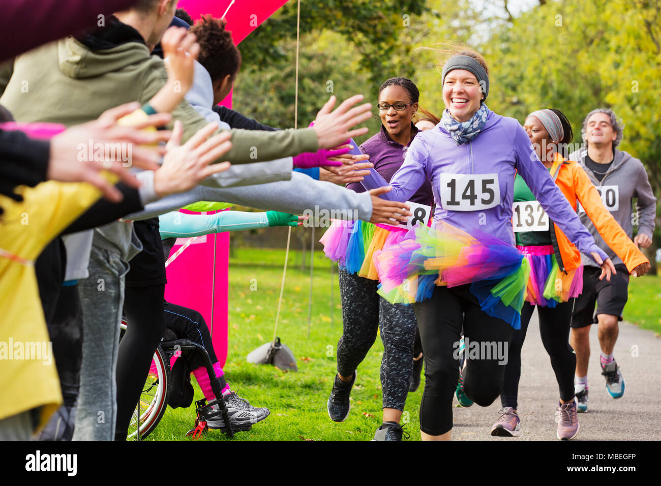 Enthusiastic female runners in tutus high-fiving spectators at charity run in park Stock Photo