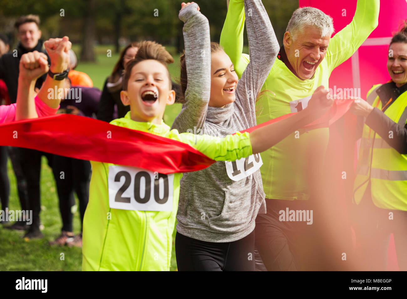 Enthusiastic boy runner crossing charity run finish line with family Stock Photo