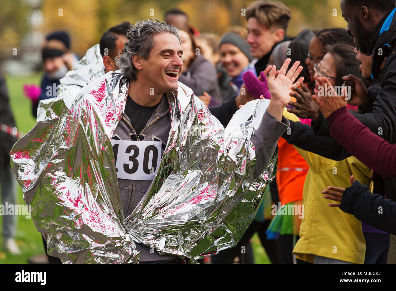Enthusiastic male marathon runner in thermal blanket high-fiving spectators Stock Photo