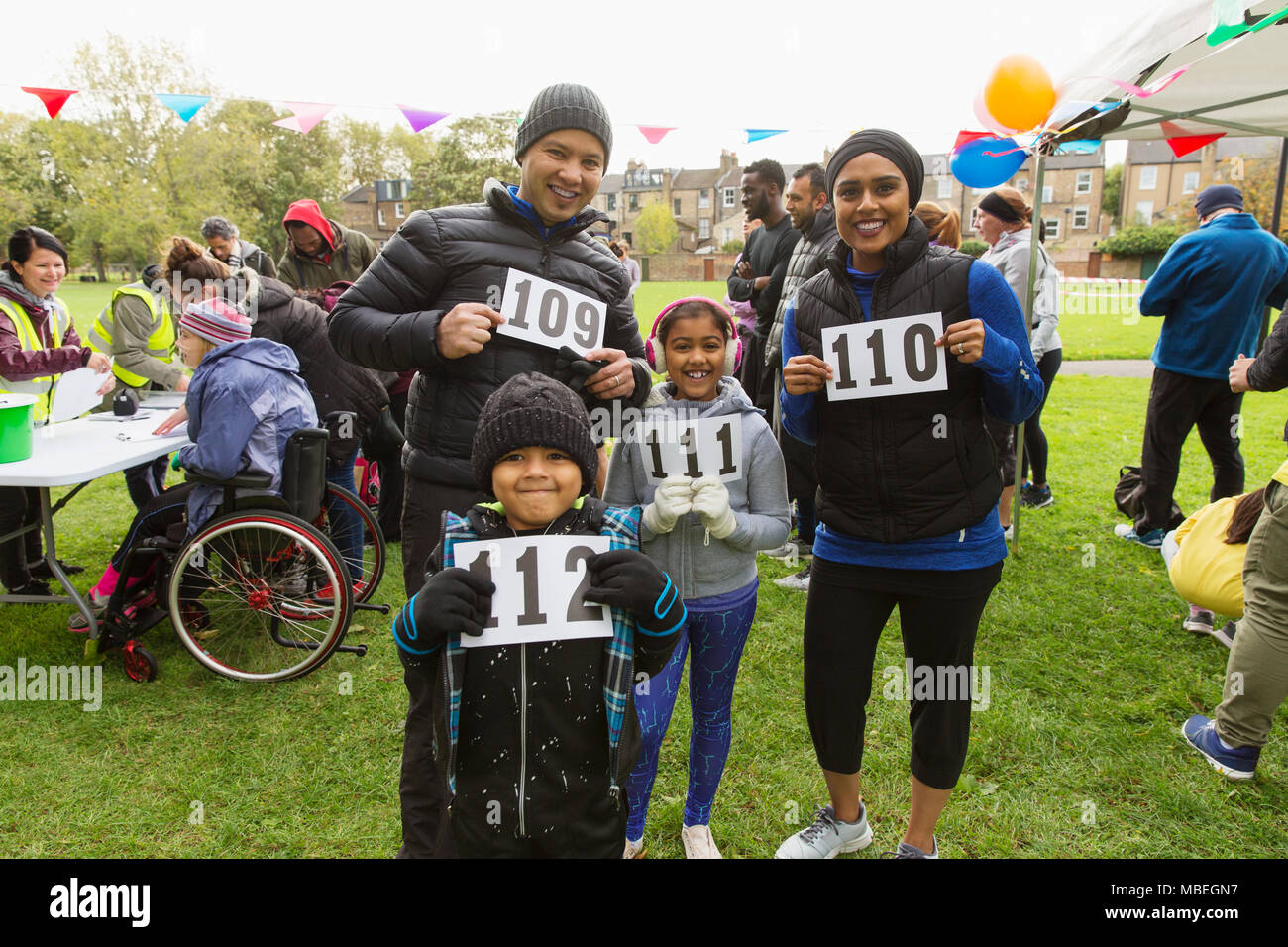 Portrait confident family runners showing marathon bibs at charity run in park Stock Photo