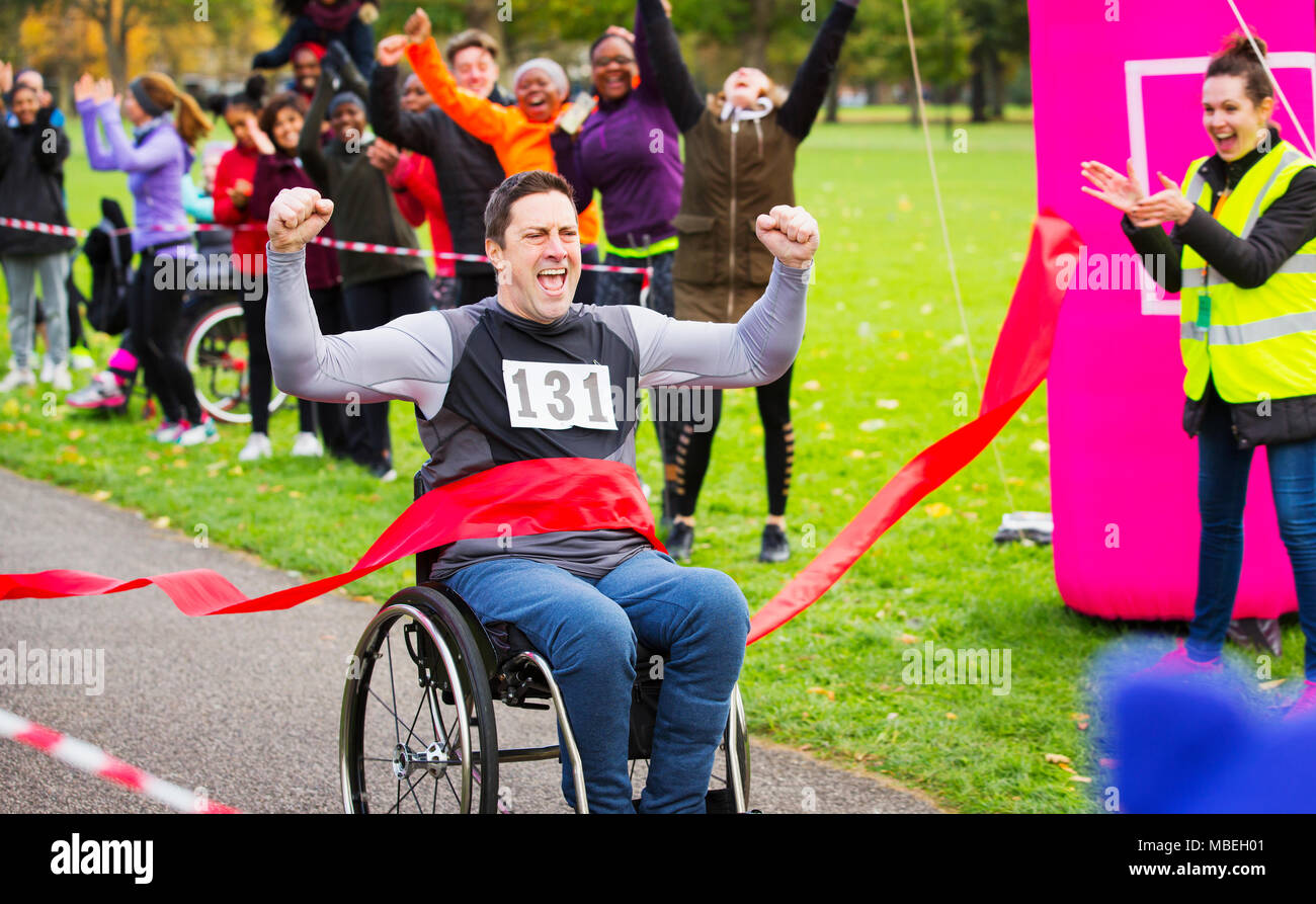 Enthusiastic man in wheelchair crossing finish line at charity race in park Stock Photo