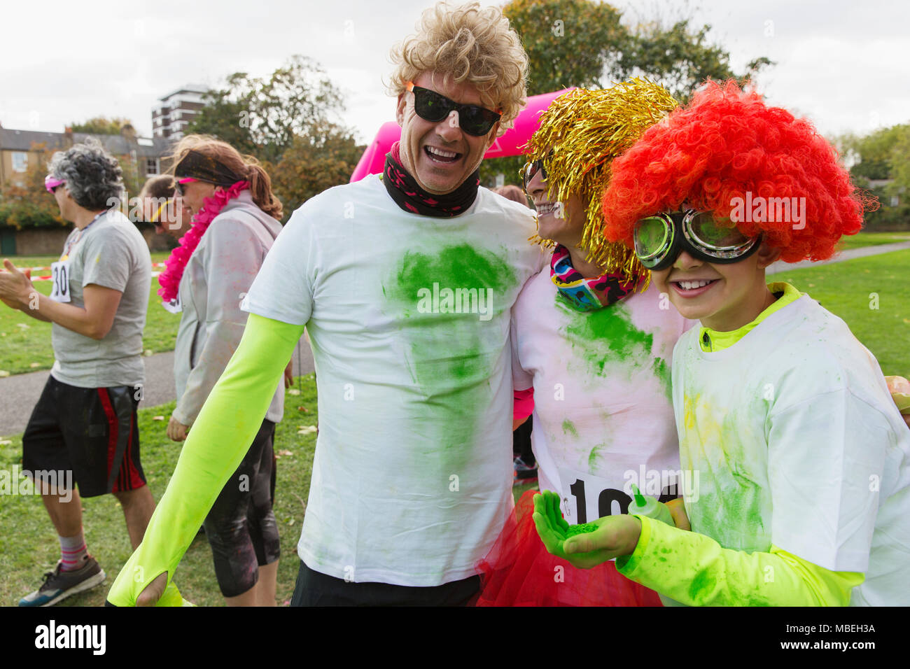 Portrait playful runners in wigs and holi powder at charity run in park Stock Photo