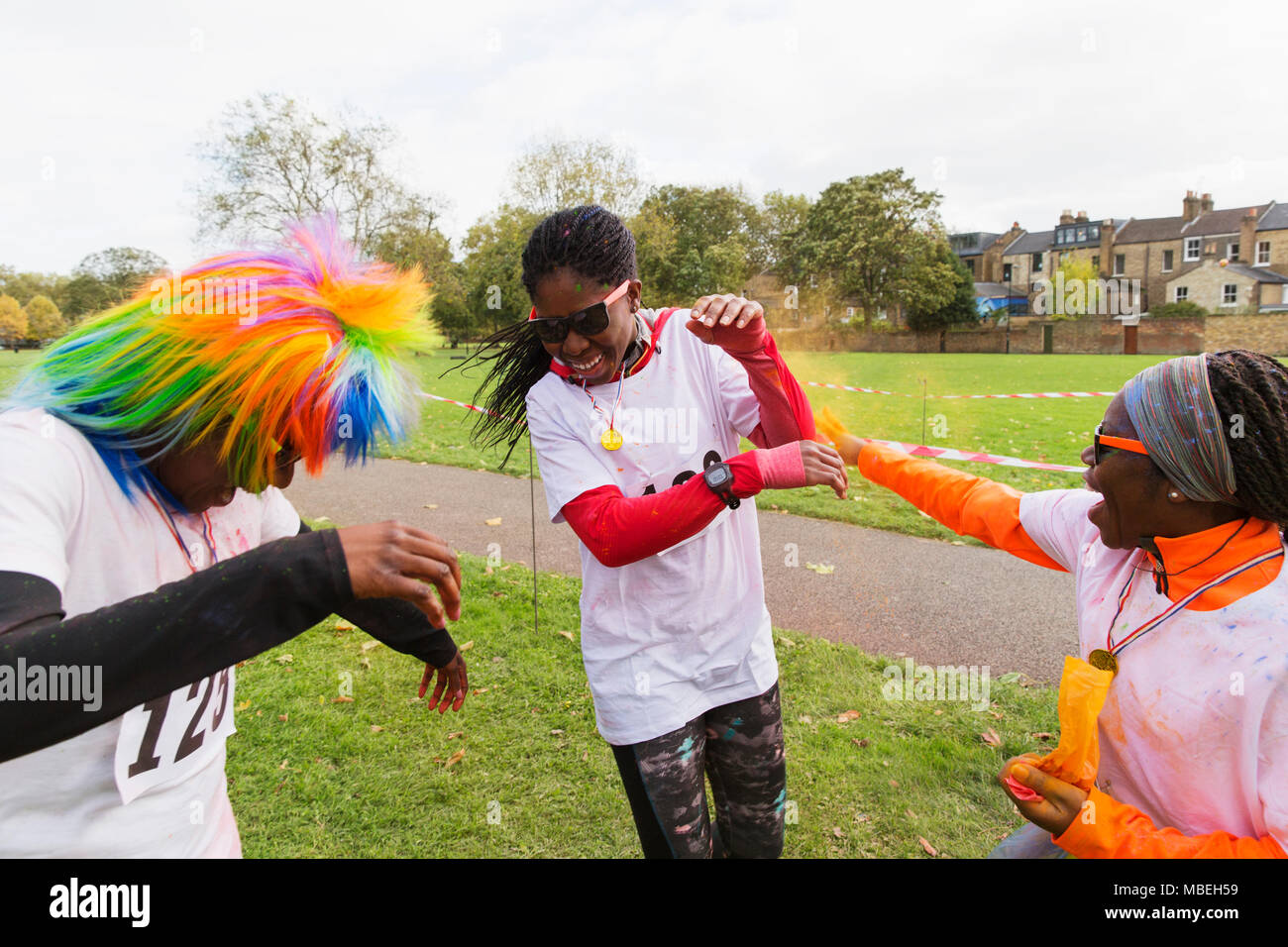 Playful runners celebrating, throwing holi powder at charity run in park Stock Photo
