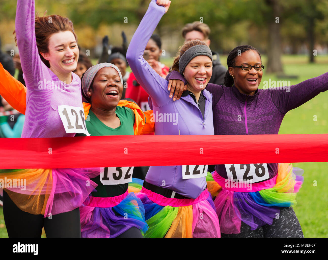Women friend runners in tutus running, crossing charity run finish line Stock Photo