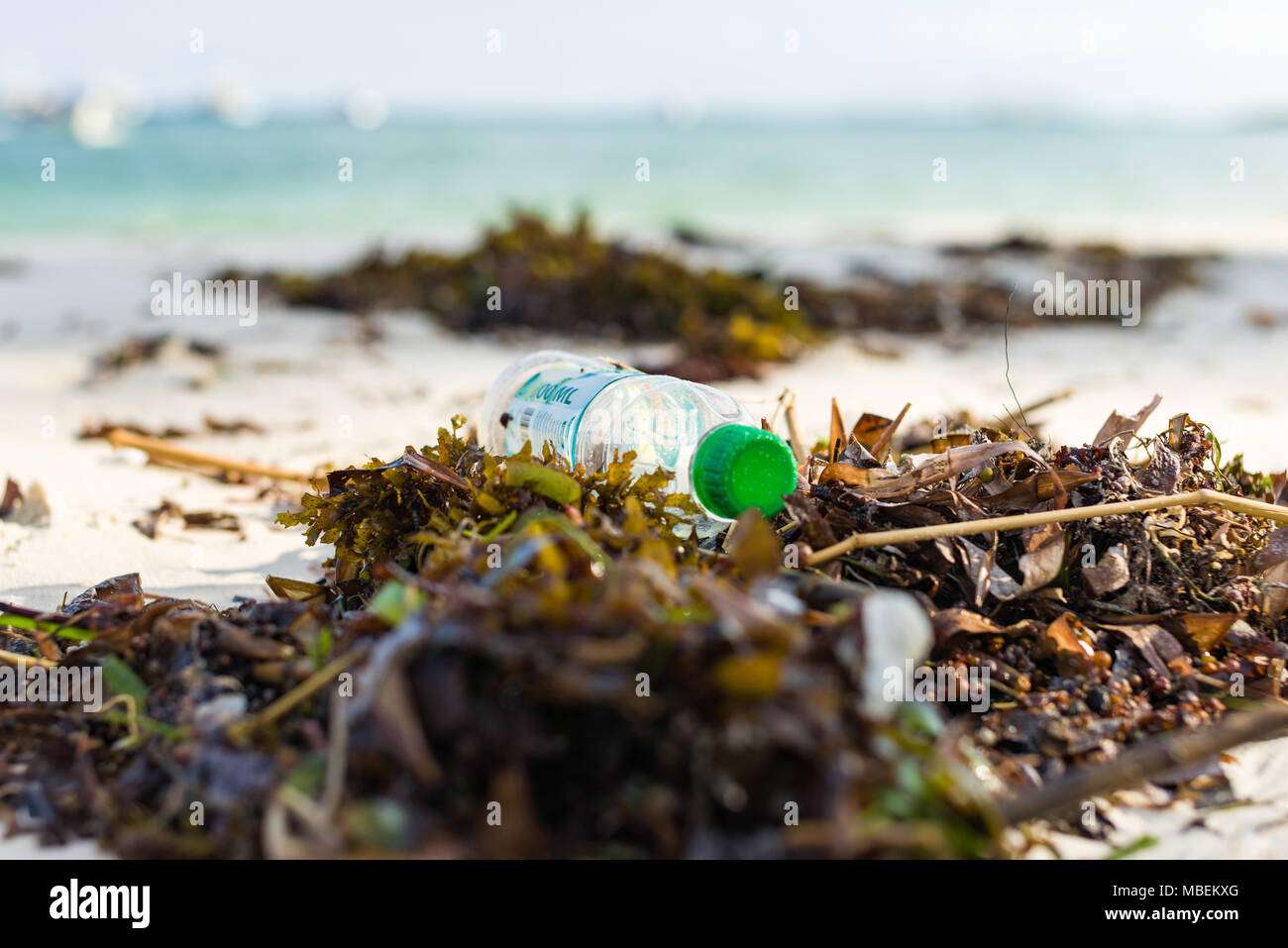 Plastic bottle waste lies washed up on the shore of a white sand beach Stock Photo