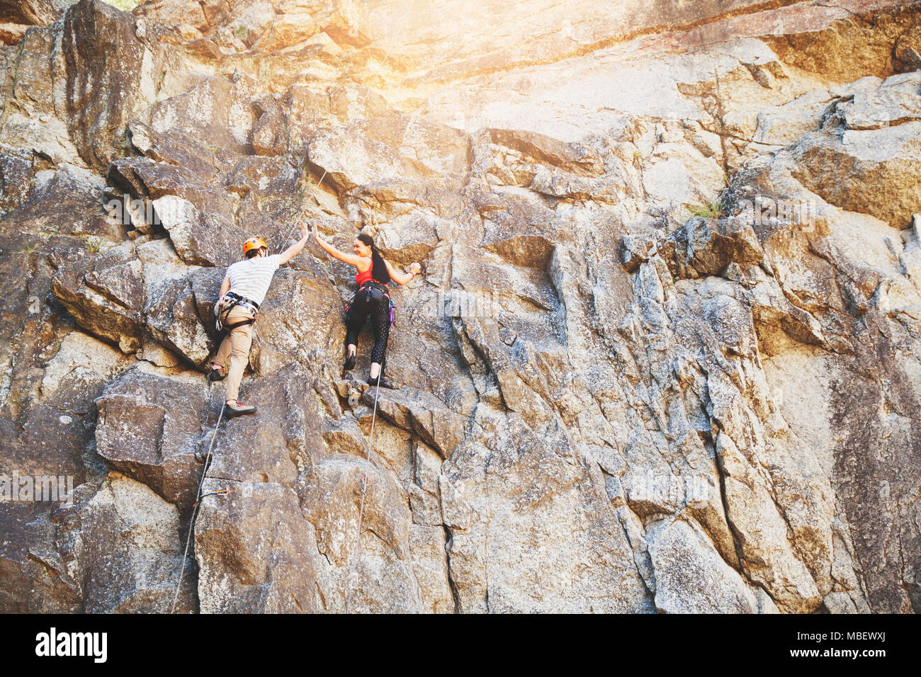 Rock climbers high-fiving on rock wall Stock Photo