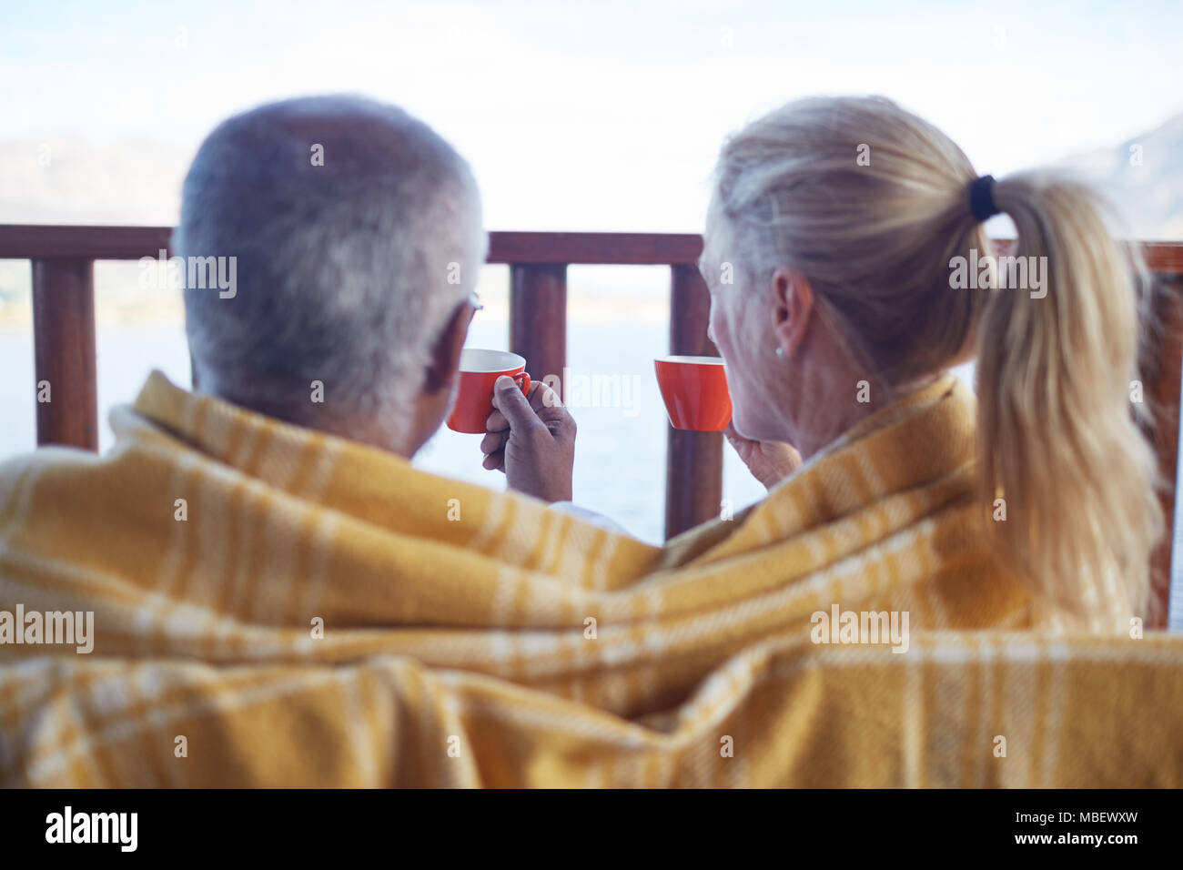 Cozy couple wrapped in blanket, drinking coffee on balcony Stock Photo