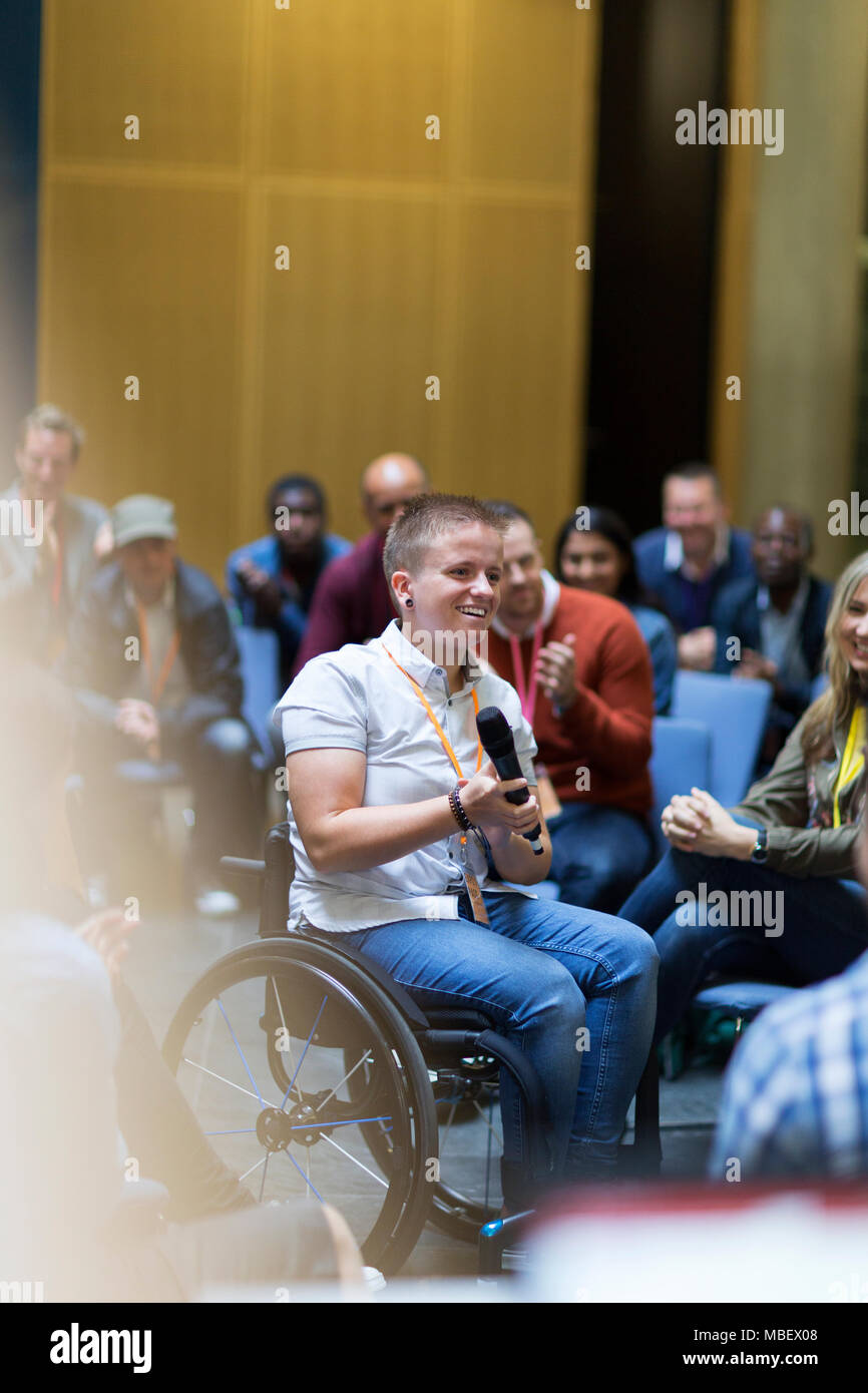 Smiling woman in wheelchair speaking with microphone in audience Stock Photo