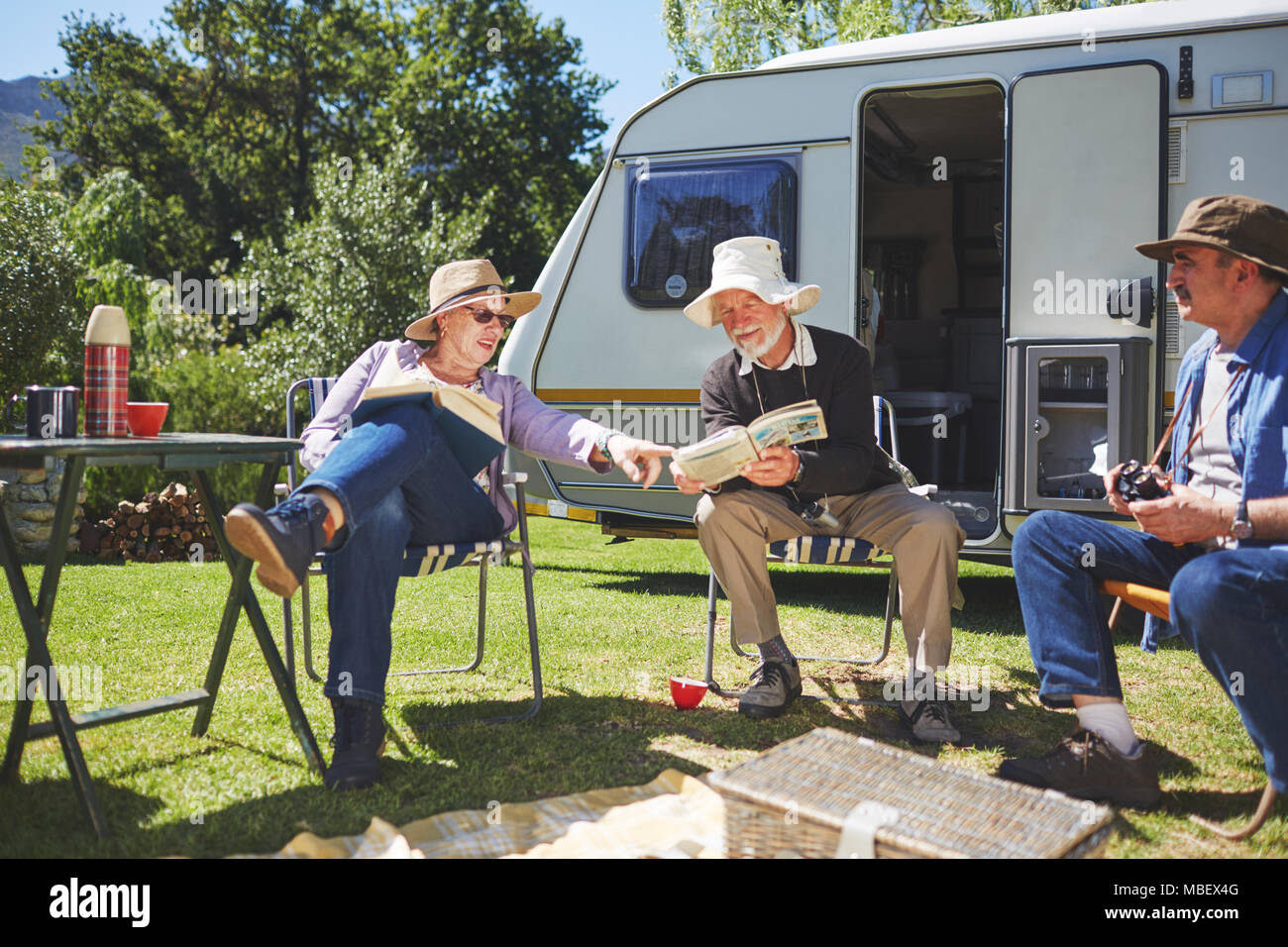 Active senior friends reading outside camper van at sunny summer campsite Stock Photo