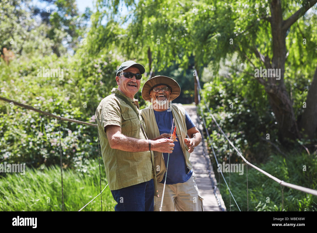 Portrait happy active senior men friends fishing on sunny summer footbridge Stock Photo