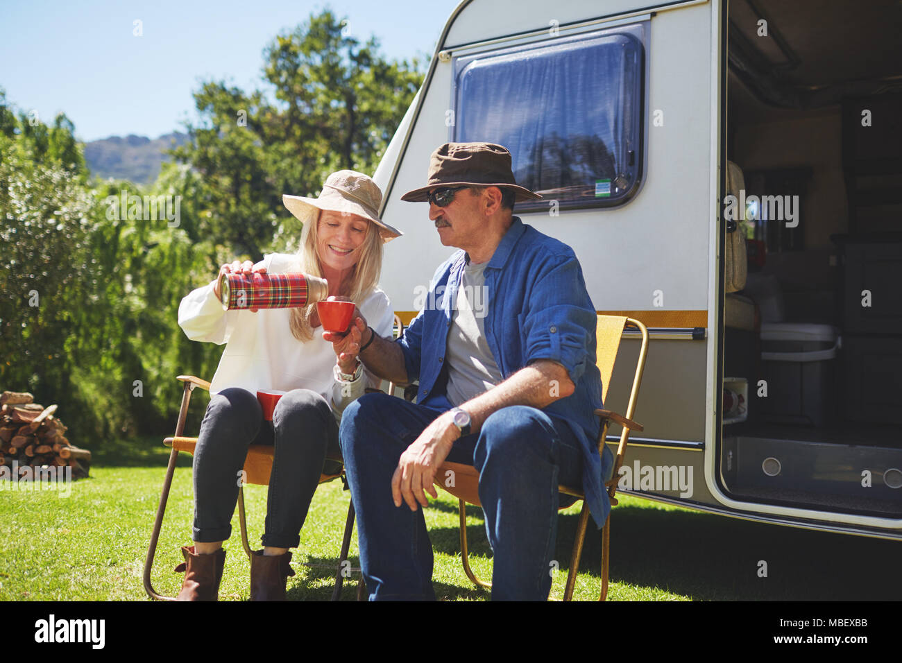 Active senior couple drinking coffee outside camper van at sunny summer campsite Stock Photo