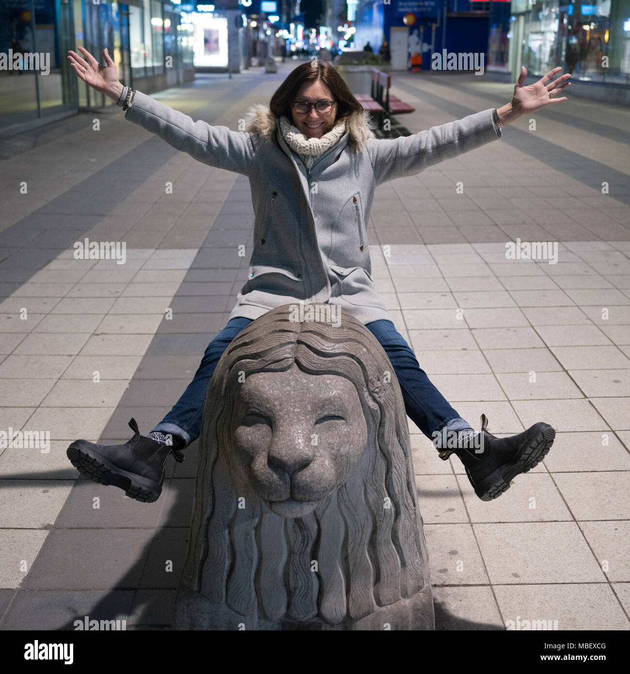 Happy woman sitting on lion sculpture, Drottninggatan Street, Stockholm, Sweden Stock Photo