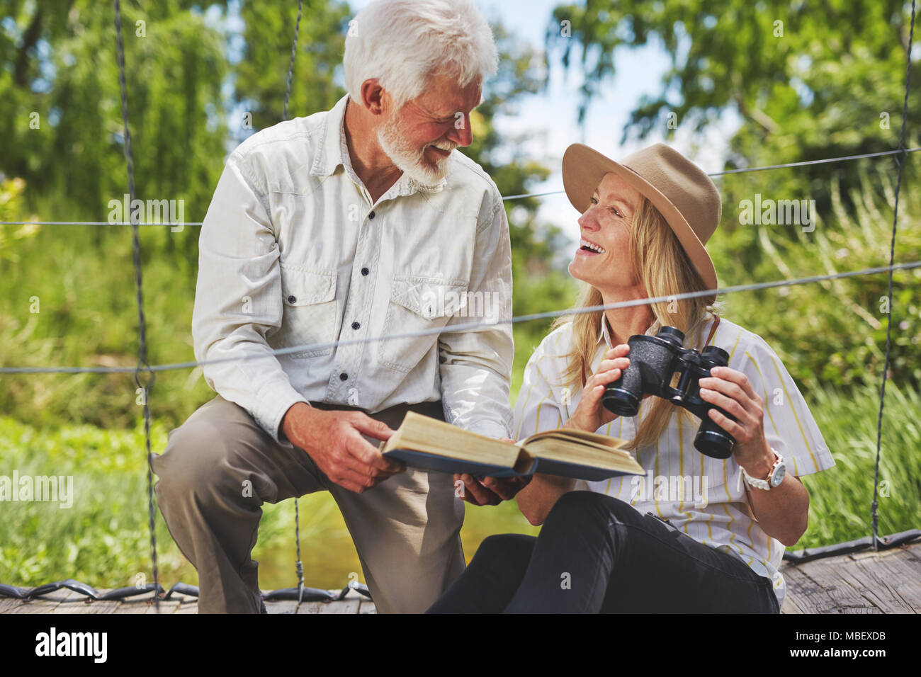 Smiling active senior couple bird watching with binoculars and book Stock Photo