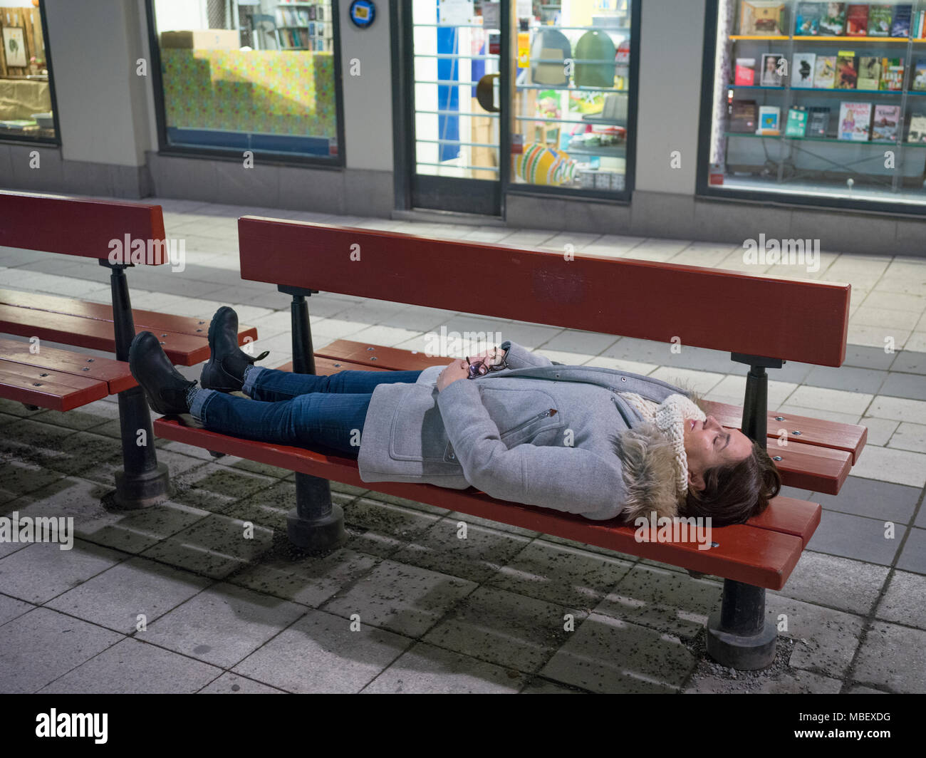 Woman sleeping on bench, Drottninggatan Street, Stockholm, Sweden Stock Photo