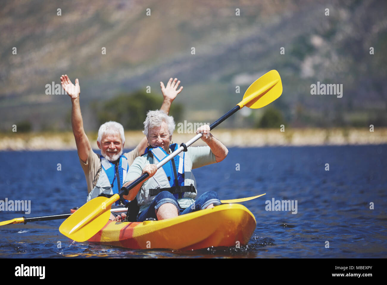 Playful, energetic active senior couple kayaking on sunny summer lake Stock Photo