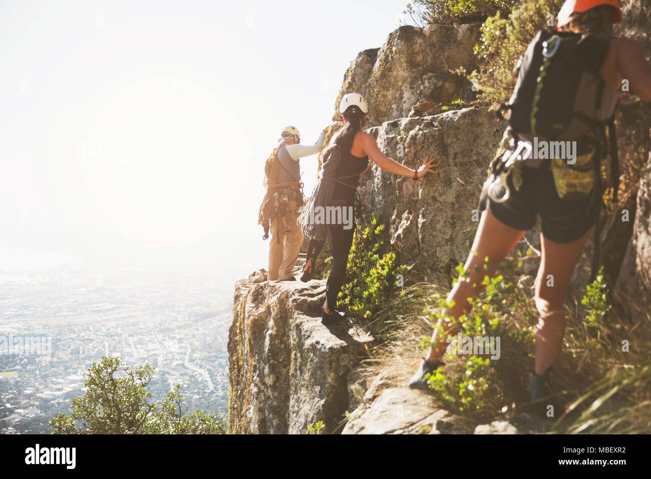 Rock climbers climbing rocks above sunny ocean Stock Photo
