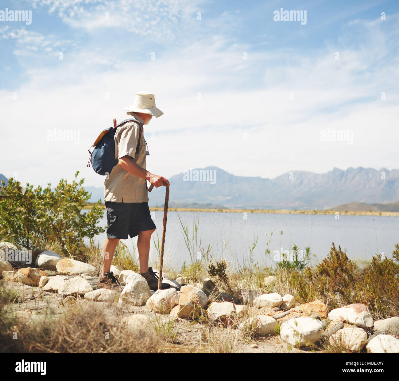 Male hiker with backpack and walking stick at sunny summer lakeside Stock Photo