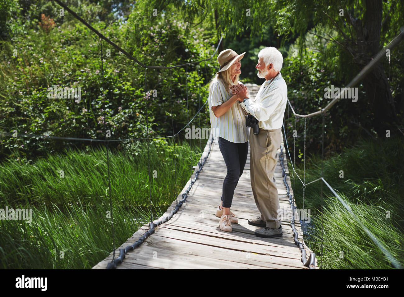 Romantic active senior couple holding hands on idyllic footbridge Stock Photo