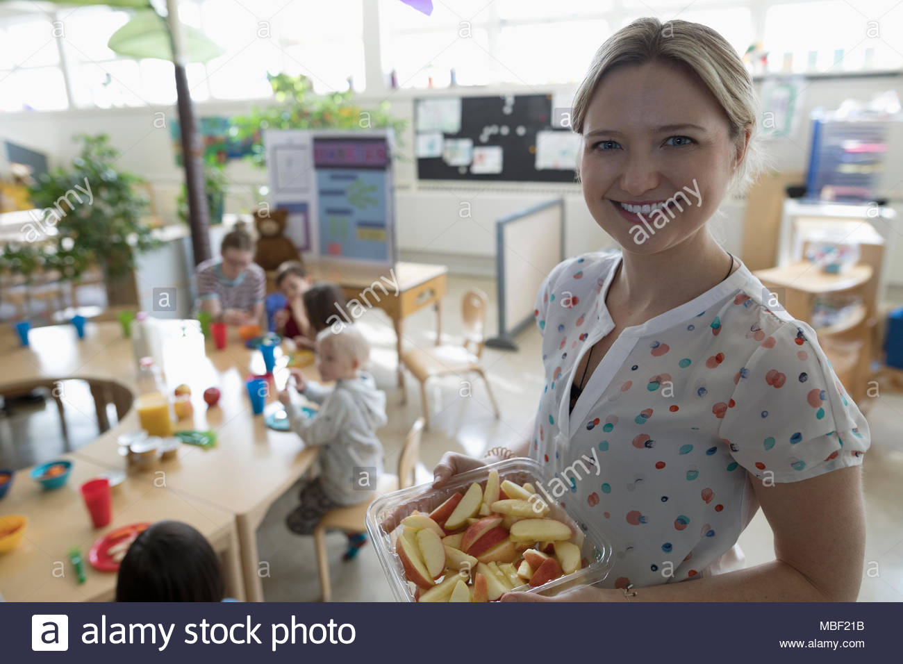Portrait smiling, confident preschool teacher serving apple slices during snack time in classroom Stock Photo