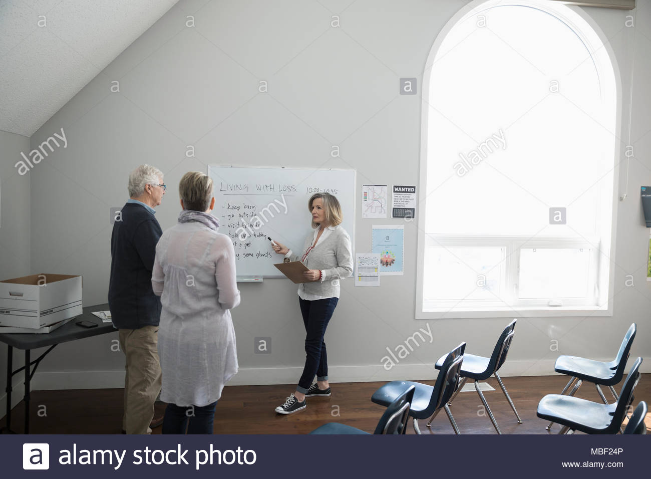 Woman at whiteboard leading grief counseling support group in community center Stock Photo