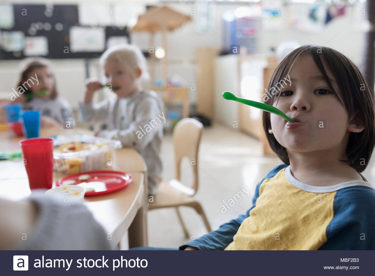 Portrait playful preschool boy with spoon eating during snack time