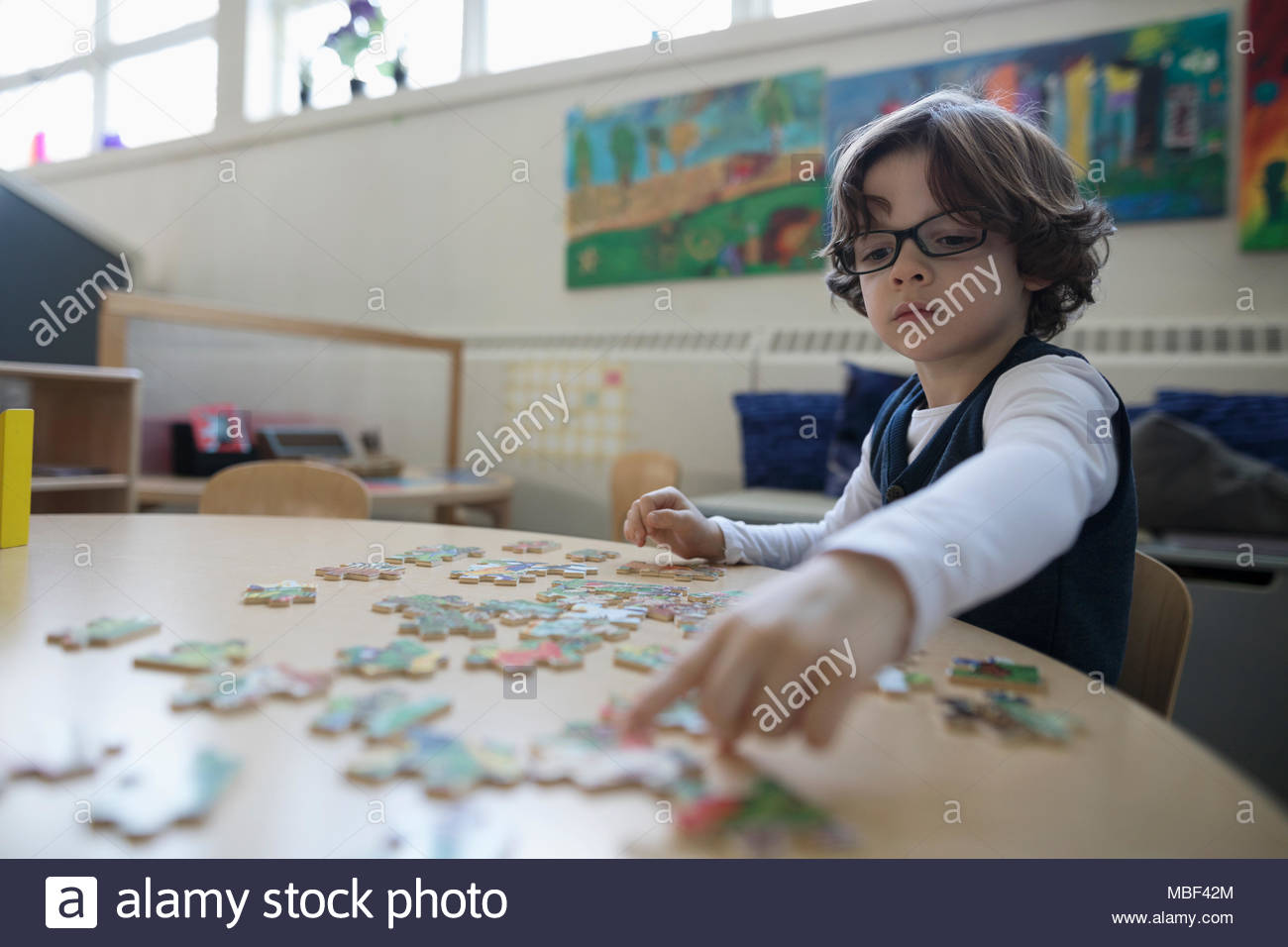 Focused preschool boy assembling jigsaw puzzle in classroom Stock Photo