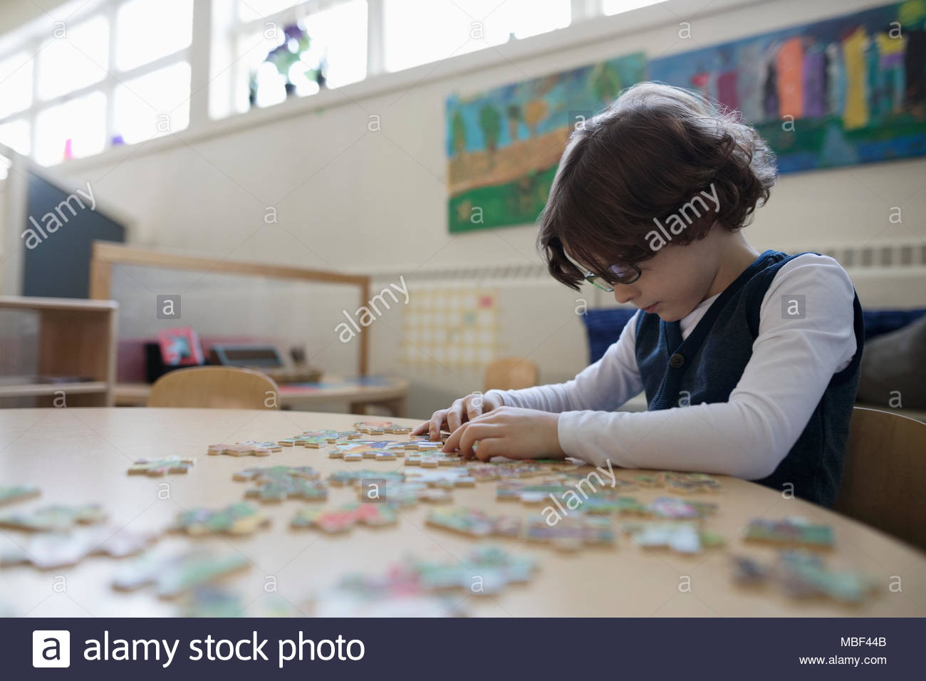 Focused preschool boy assembling jigsaw puzzle in classroom Stock Photo