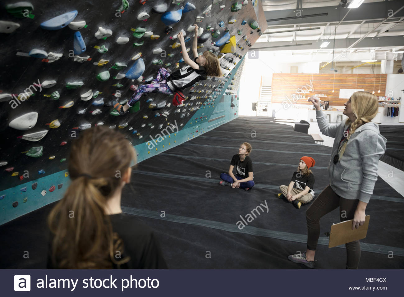 Female instructor teaching girl rock climber students at climbing wall in climbing gym Stock