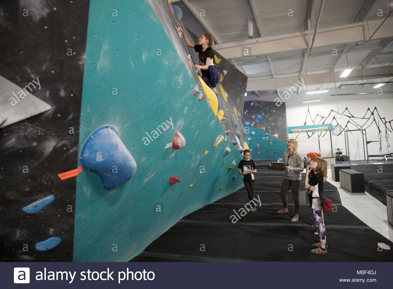 Female instructor and rock climbing students watching girl climbing