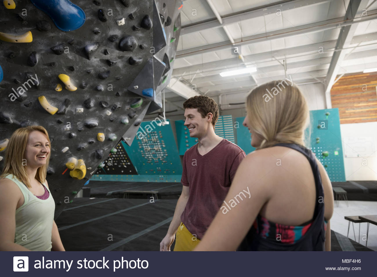 Happy rock climber friends talking at climbing wall in climbing gym Stock Photo