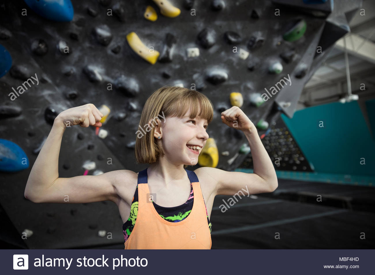Confident, strong, tough, smiling girl rock climber flexing muscles at